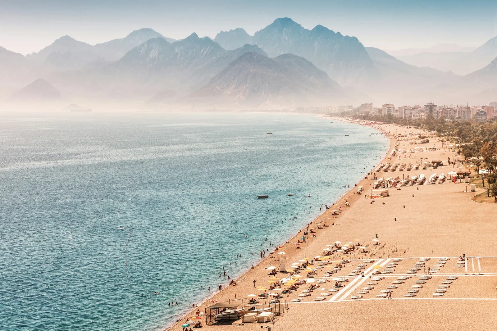 The long Konyaalti beach curving toward the Taurus mountains in soft haze.