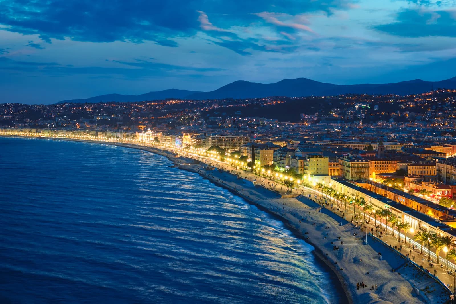 The Promenade des Anglais curving along Nice's bay at blue hour with city lights reflected on the sea.