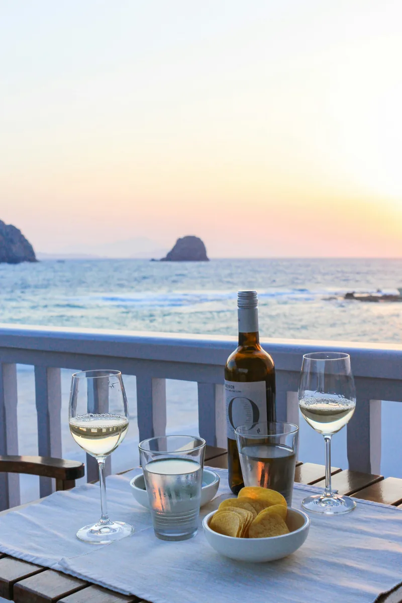 White wine bottle and two glasses on a balcony table at dusk over the sea.